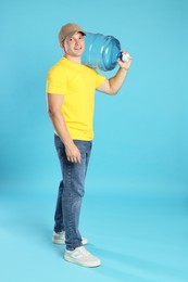 Photo of Smiling delivery man with cooler bottle of water on light blue background