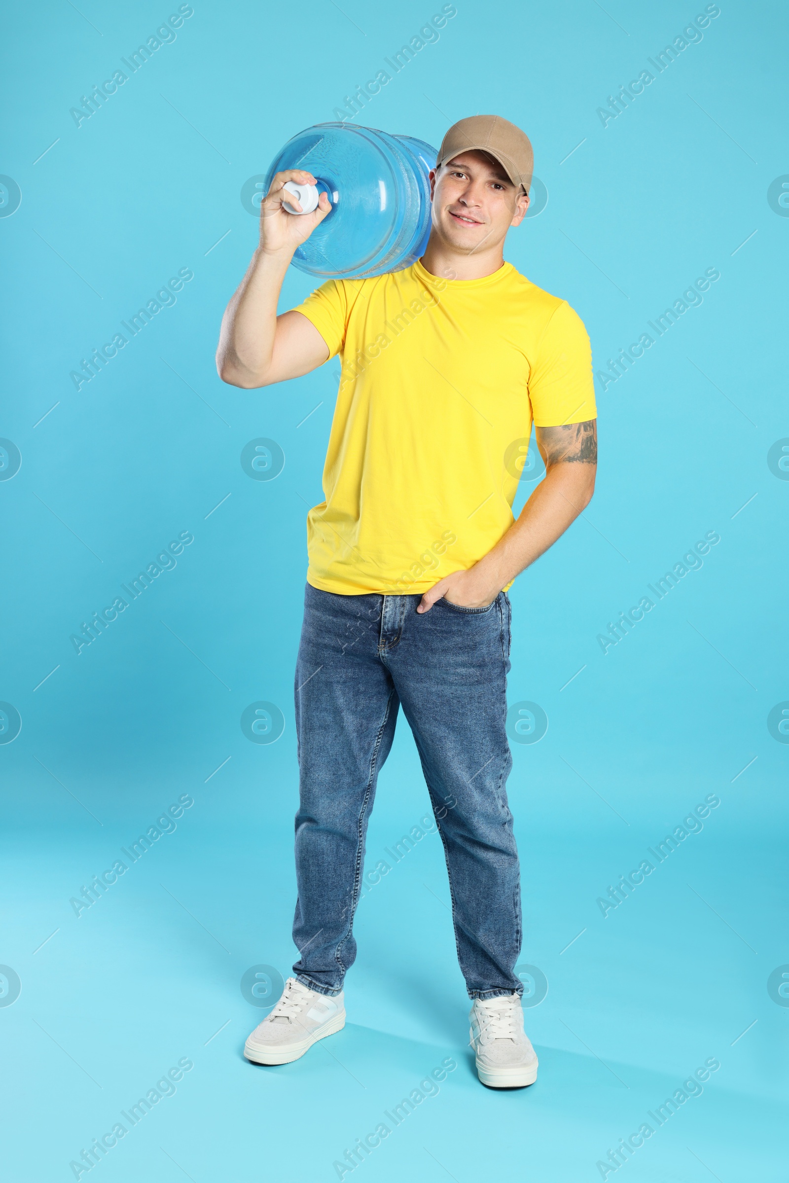 Photo of Smiling delivery man with cooler bottle of water on light blue background