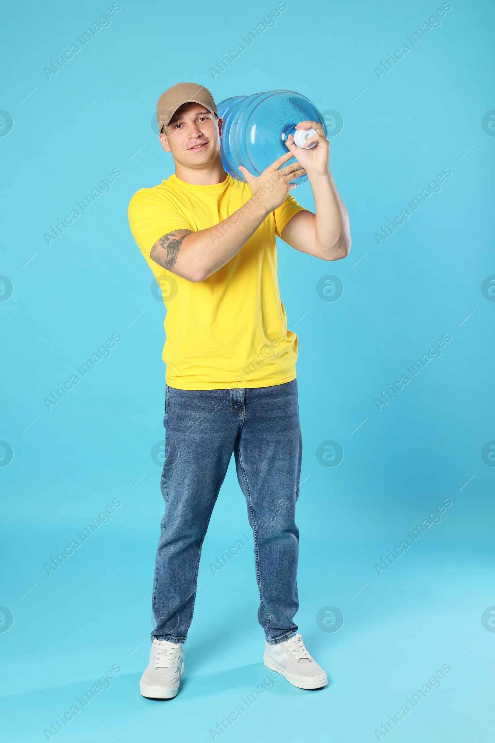 Photo of Smiling delivery man with cooler bottle of water on light blue background