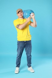 Photo of Smiling delivery man with cooler bottle of water on light blue background