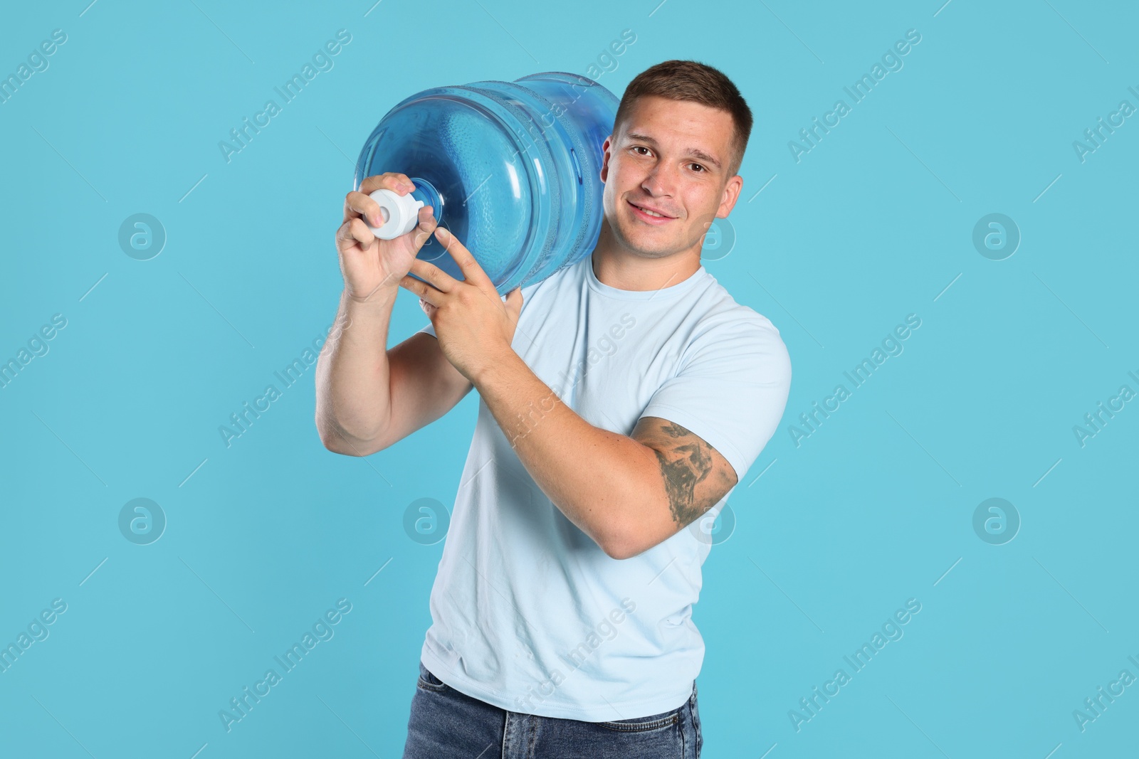 Photo of Smiling delivery man with cooler bottle of water on light blue background