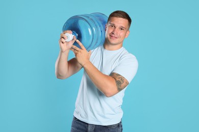 Photo of Smiling delivery man with cooler bottle of water on light blue background
