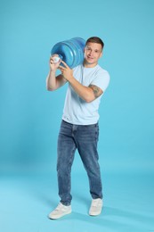 Photo of Smiling delivery man with cooler bottle of water on light blue background