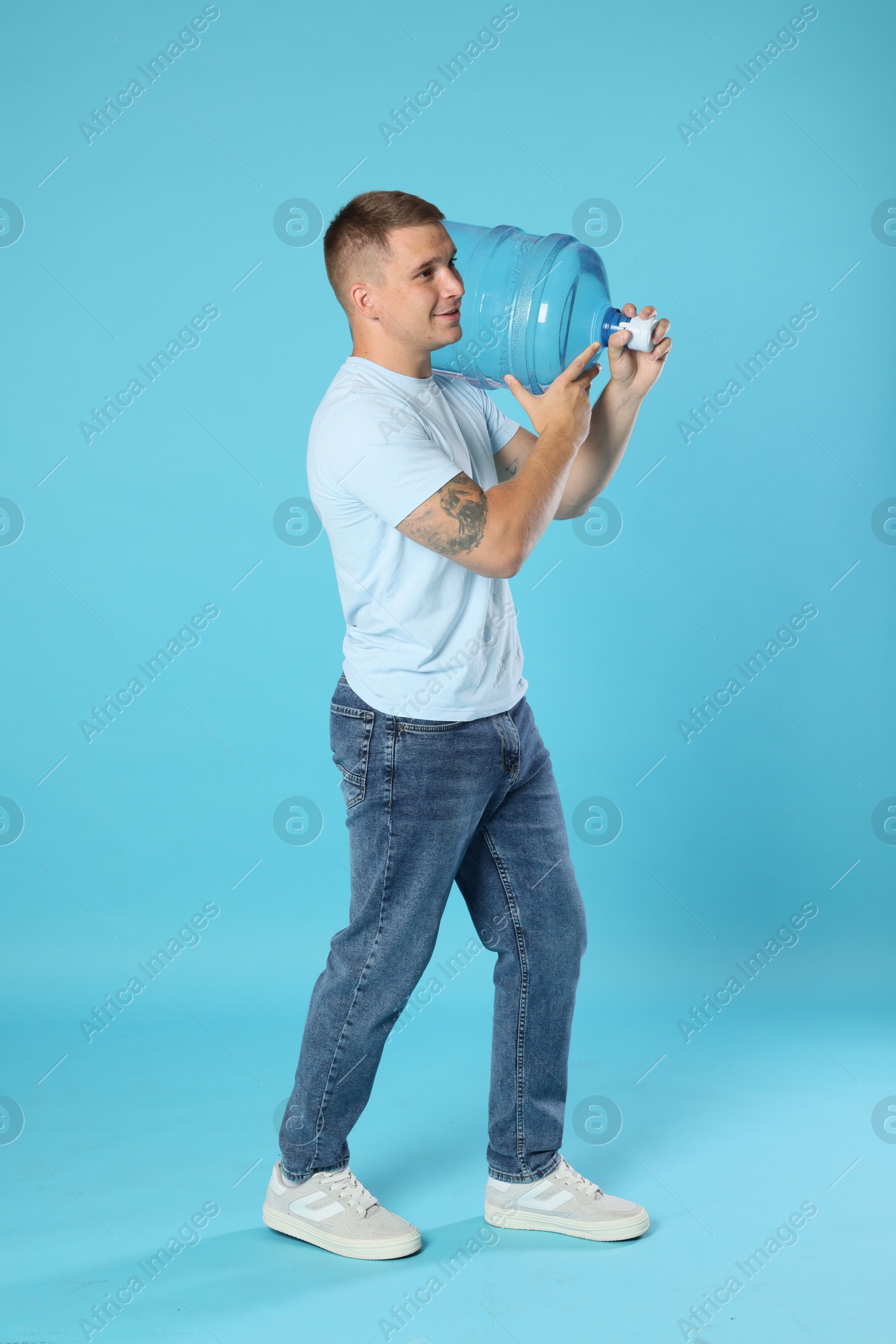 Photo of Delivery man with cooler bottle of water on light blue background