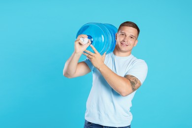 Photo of Smiling delivery man with cooler bottle of water on light blue background