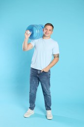 Photo of Smiling delivery man with cooler bottle of water on light blue background