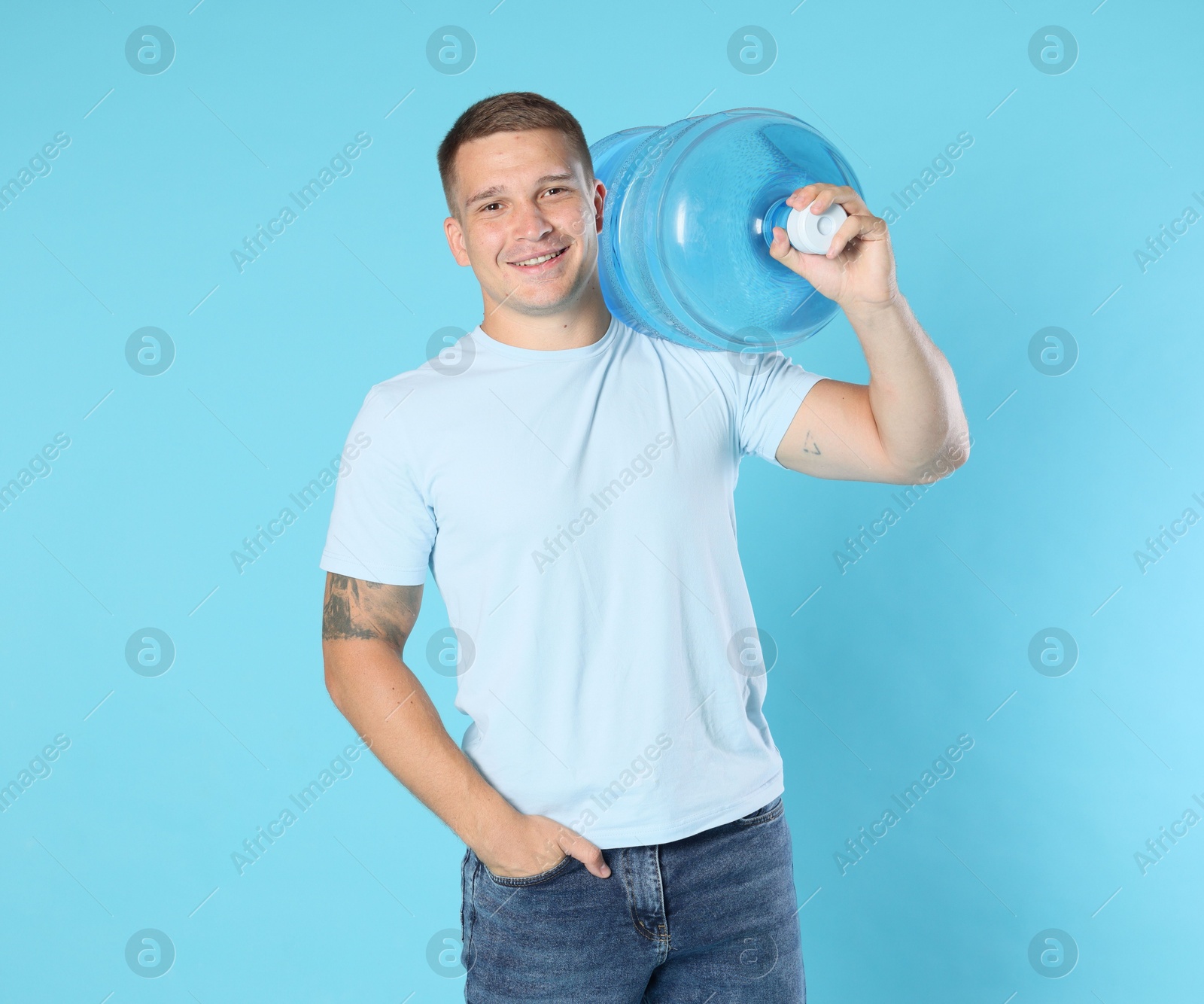 Photo of Smiling delivery man with cooler bottle of water on light blue background