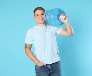 Photo of Smiling delivery man with cooler bottle of water on light blue background