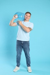 Photo of Smiling delivery man with cooler bottle of water on light blue background