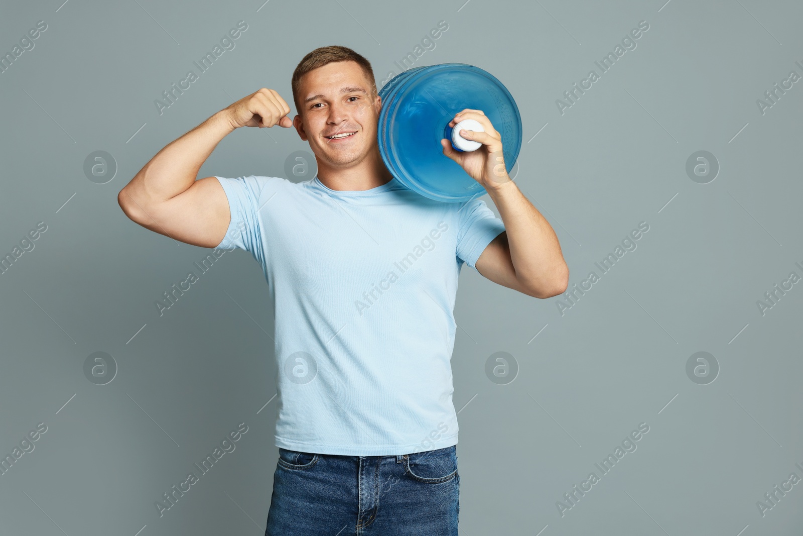 Photo of Smiling delivery man with cooler bottle of water showing his biceps on grey background