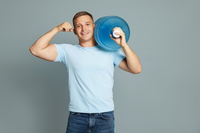 Photo of Smiling delivery man with cooler bottle of water showing his biceps on grey background