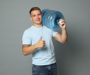 Photo of Smiling delivery man with cooler bottle of water showing thumbs up on grey background