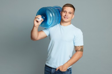 Photo of Smiling delivery man with cooler bottle of water on grey background