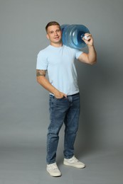 Photo of Smiling delivery man with cooler bottle of water on grey background