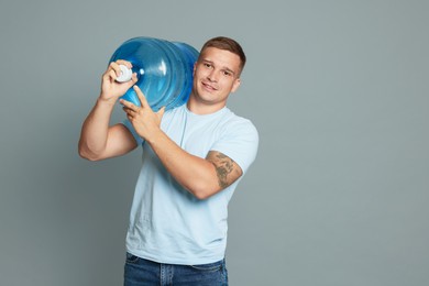 Photo of Smiling delivery man with cooler bottle of water on grey background. Space for text