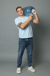 Photo of Smiling delivery man with cooler bottle of water on grey background