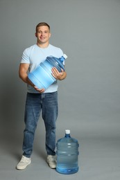 Photo of Smiling delivery man with cooler bottles of water on grey background
