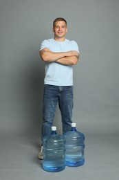 Photo of Smiling delivery man with crossed arms and cooler bottles of water on grey background
