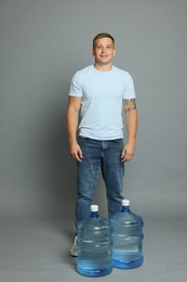Photo of Smiling delivery man and cooler bottles of water on grey background