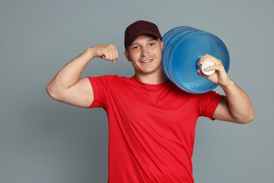 Photo of Smiling delivery man with cooler bottle of water showing his biceps on grey background