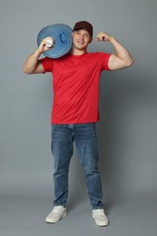 Photo of Smiling delivery man with cooler bottle of water showing his biceps on grey background