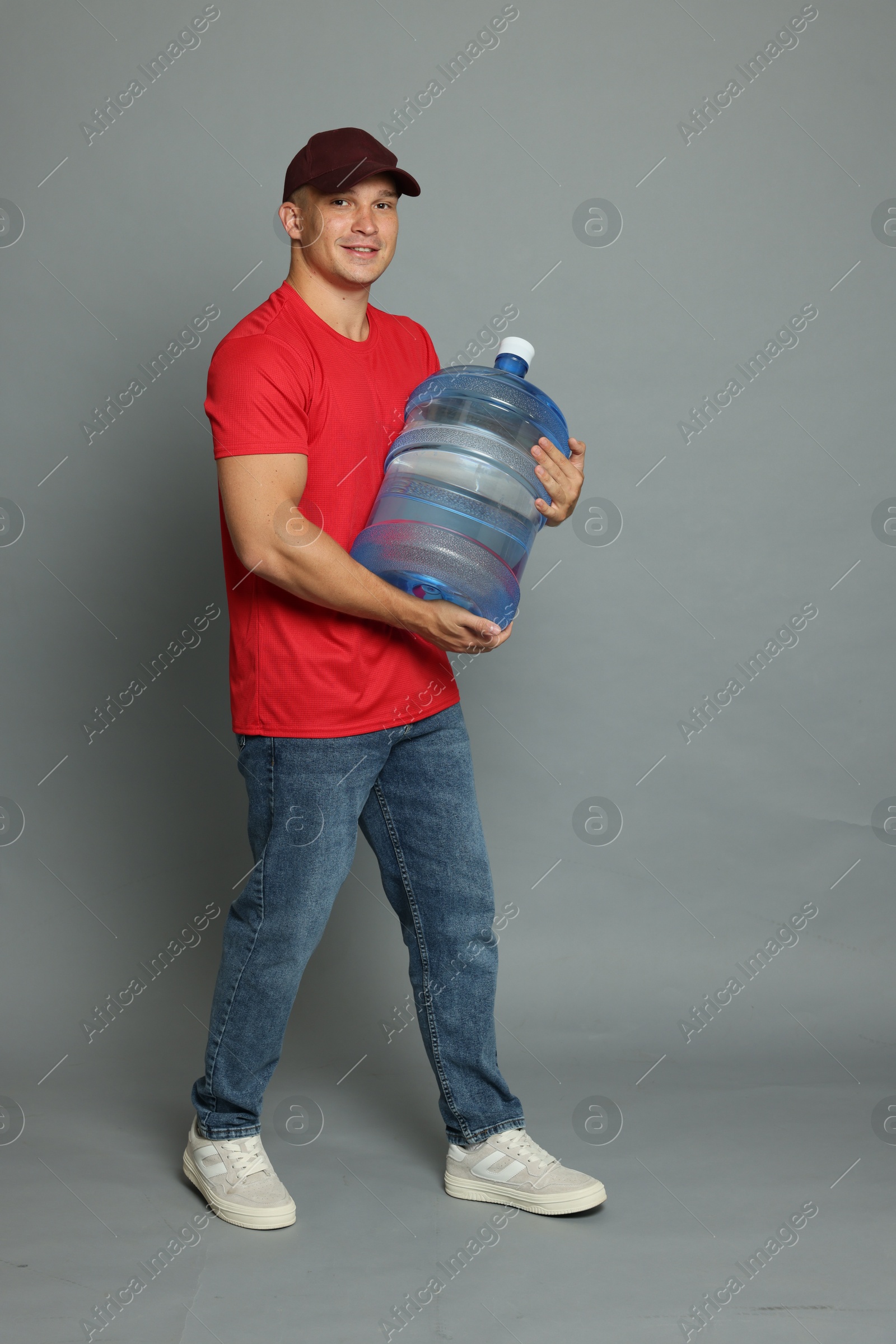 Photo of Smiling delivery man with cooler bottle of water on grey background