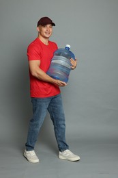 Photo of Smiling delivery man with cooler bottle of water on grey background