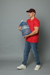 Photo of Smiling delivery man with cooler bottle of water on grey background