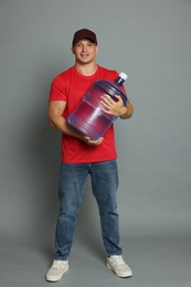 Photo of Smiling delivery man with cooler bottle of water on grey background