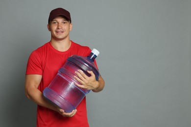 Photo of Smiling delivery man with cooler bottle of water on grey background. Space for text