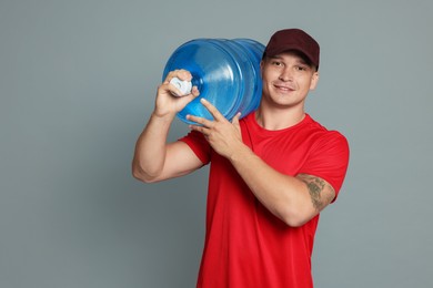 Photo of Smiling delivery man with cooler bottle of water on grey background. Space for text