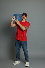 Photo of Smiling delivery man with cooler bottle of water on grey background