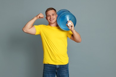 Photo of Smiling delivery man with cooler bottle of water showing his biceps on grey background