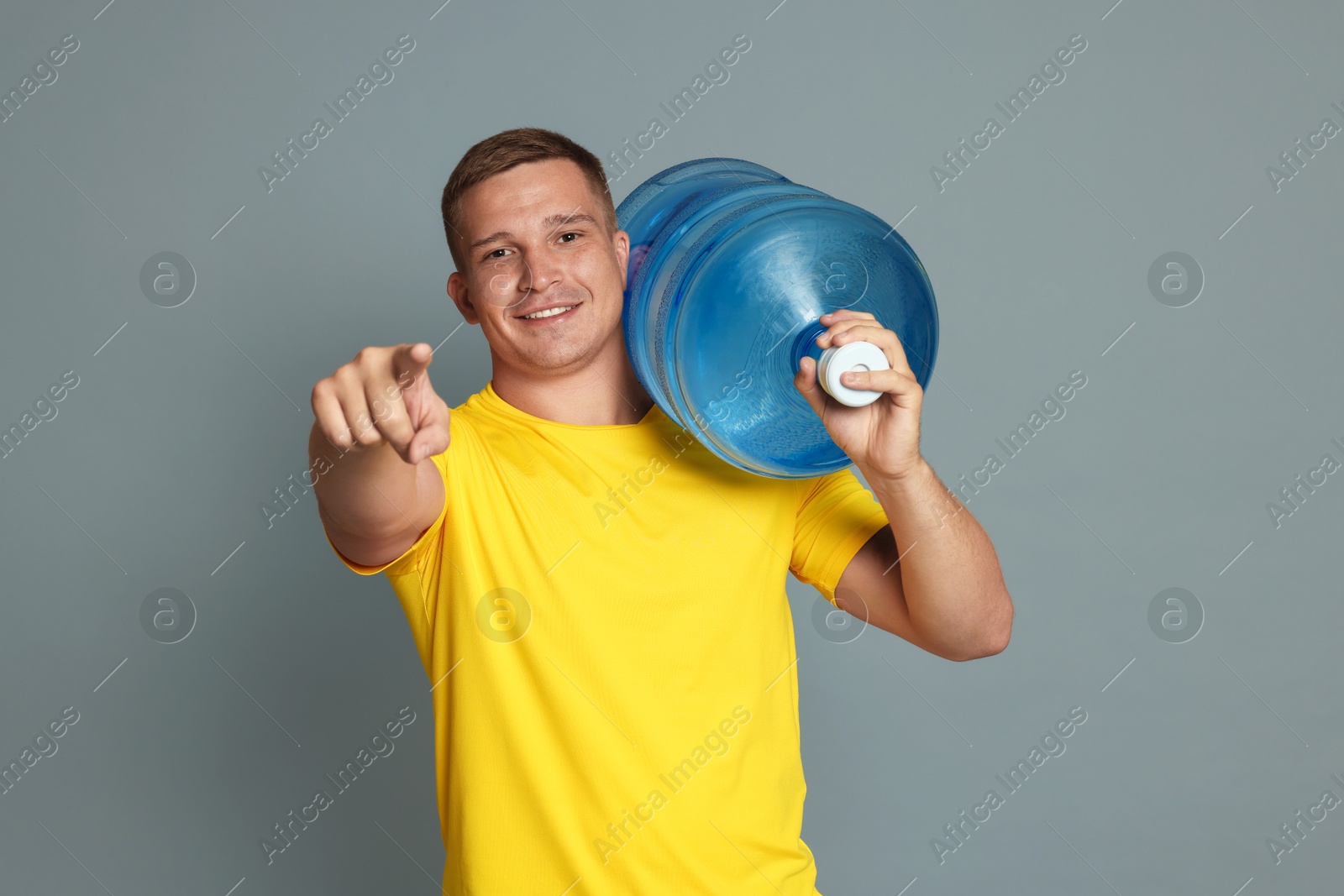 Photo of Smiling delivery man with cooler bottle of water pointing at camera on grey background