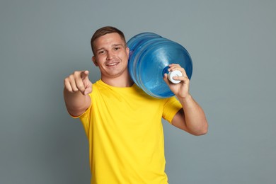 Photo of Smiling delivery man with cooler bottle of water pointing at camera on grey background