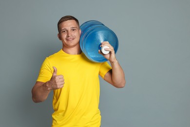 Photo of Smiling delivery man with cooler bottle of water showing thumbs up on grey background. Space for text