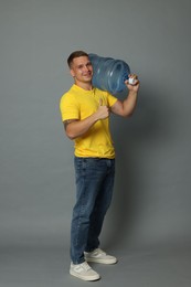 Photo of Smiling delivery man with cooler bottle of water showing thumbs up on grey background