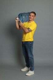 Photo of Smiling delivery man with cooler bottle of water on grey background