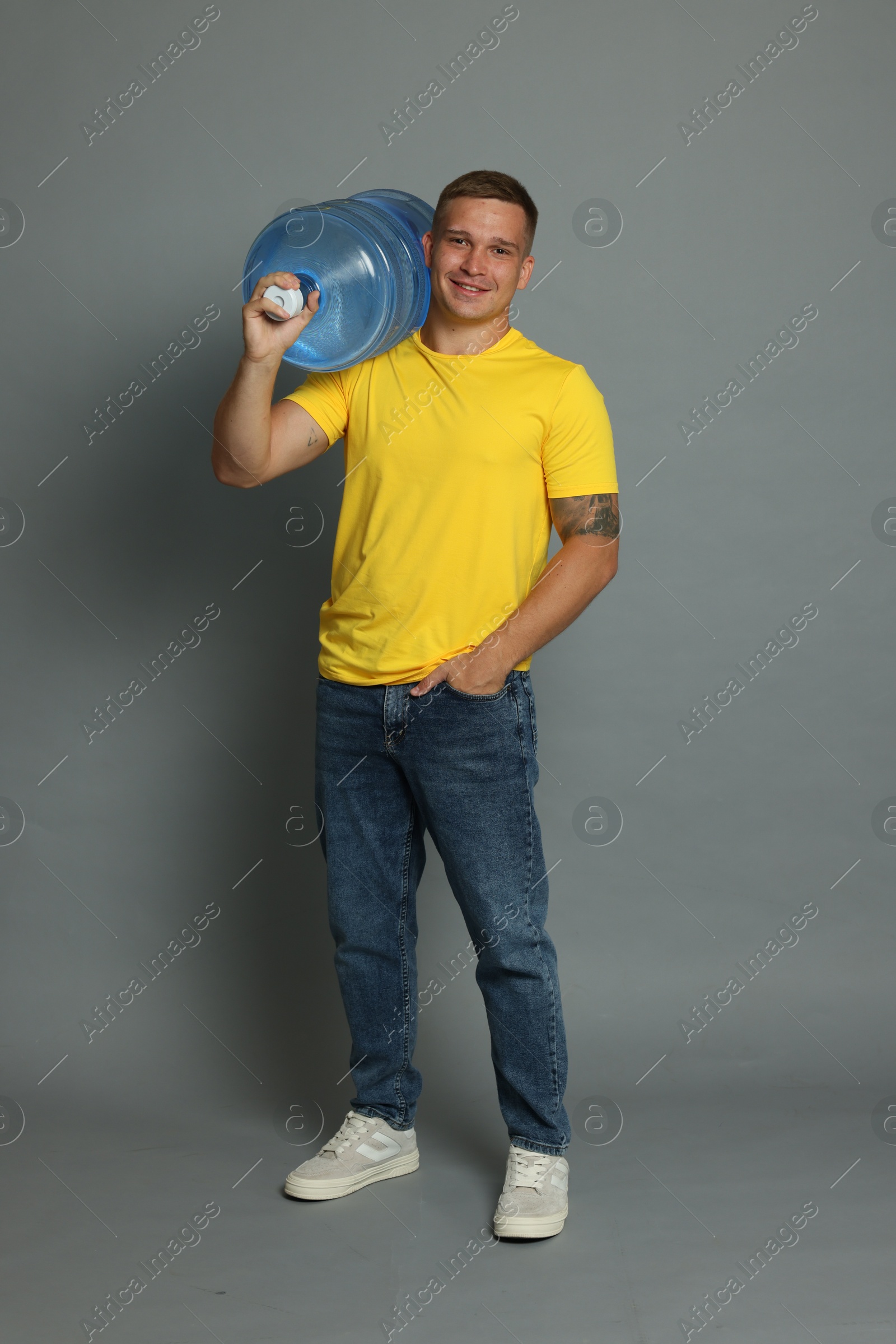 Photo of Smiling delivery man with cooler bottle of water on grey background