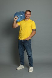 Photo of Smiling delivery man with cooler bottle of water on grey background