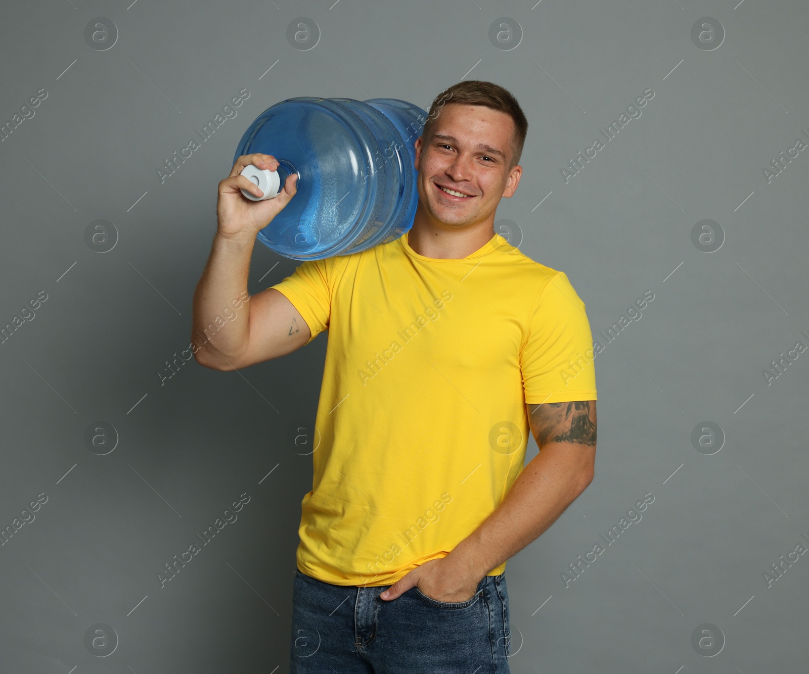 Photo of Smiling delivery man with cooler bottle of water on grey background