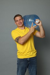 Photo of Smiling delivery man with cooler bottle of water on grey background