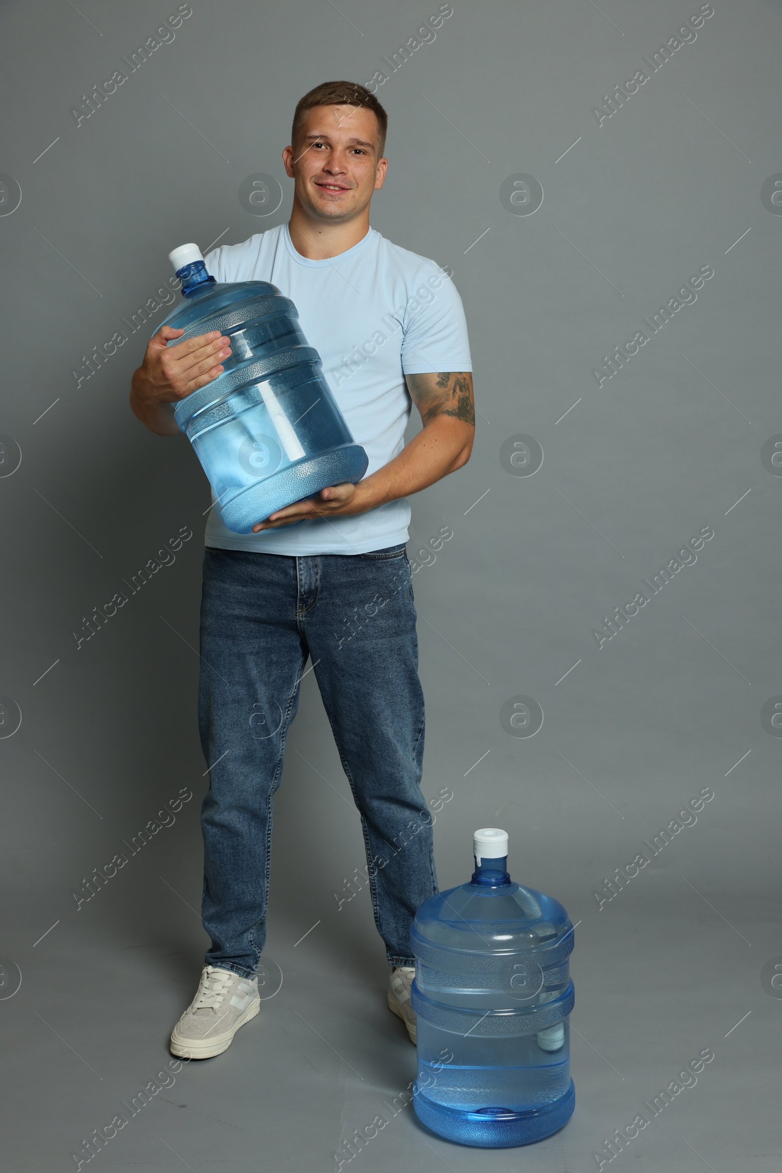 Photo of Smiling delivery man with cooler bottles of water on grey background