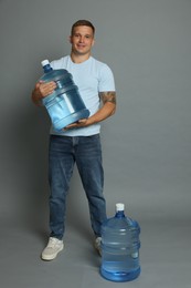 Photo of Smiling delivery man with cooler bottles of water on grey background