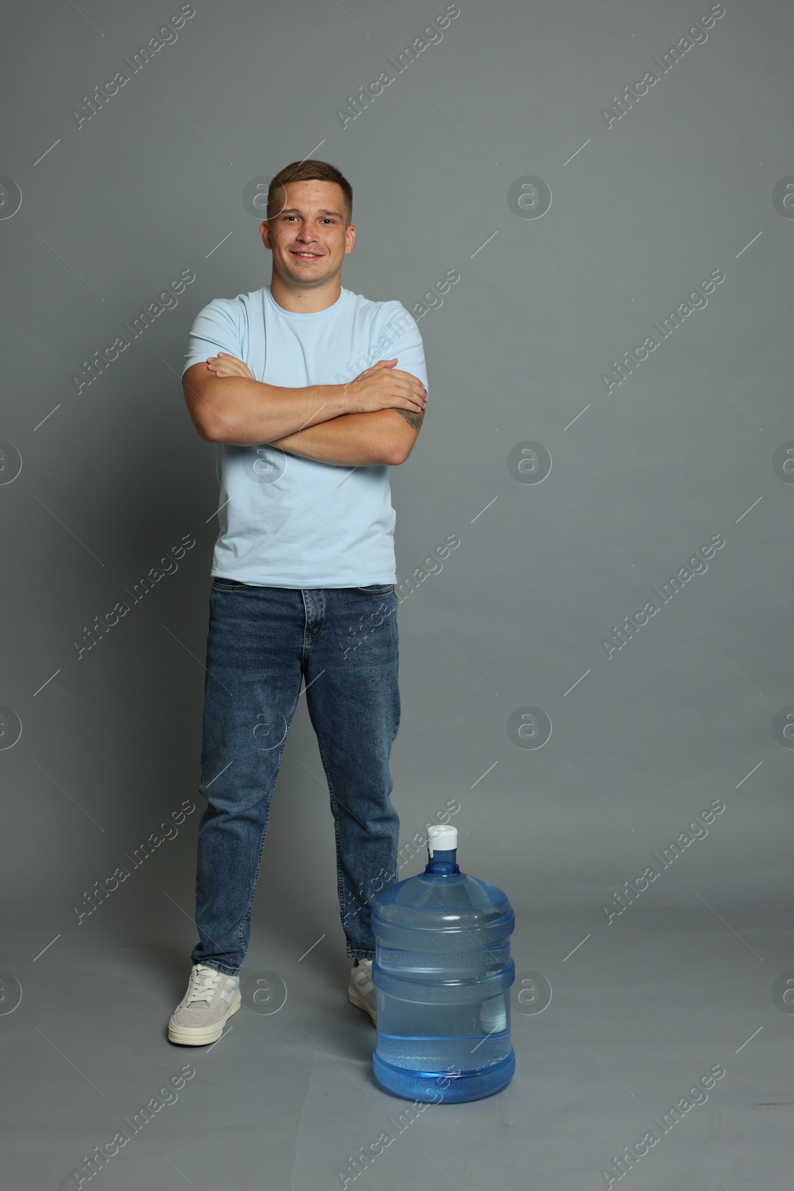 Photo of Smiling delivery man with crossed arms and cooler bottle of water on grey background