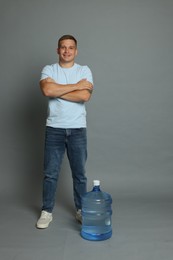 Photo of Smiling delivery man with crossed arms and cooler bottle of water on grey background