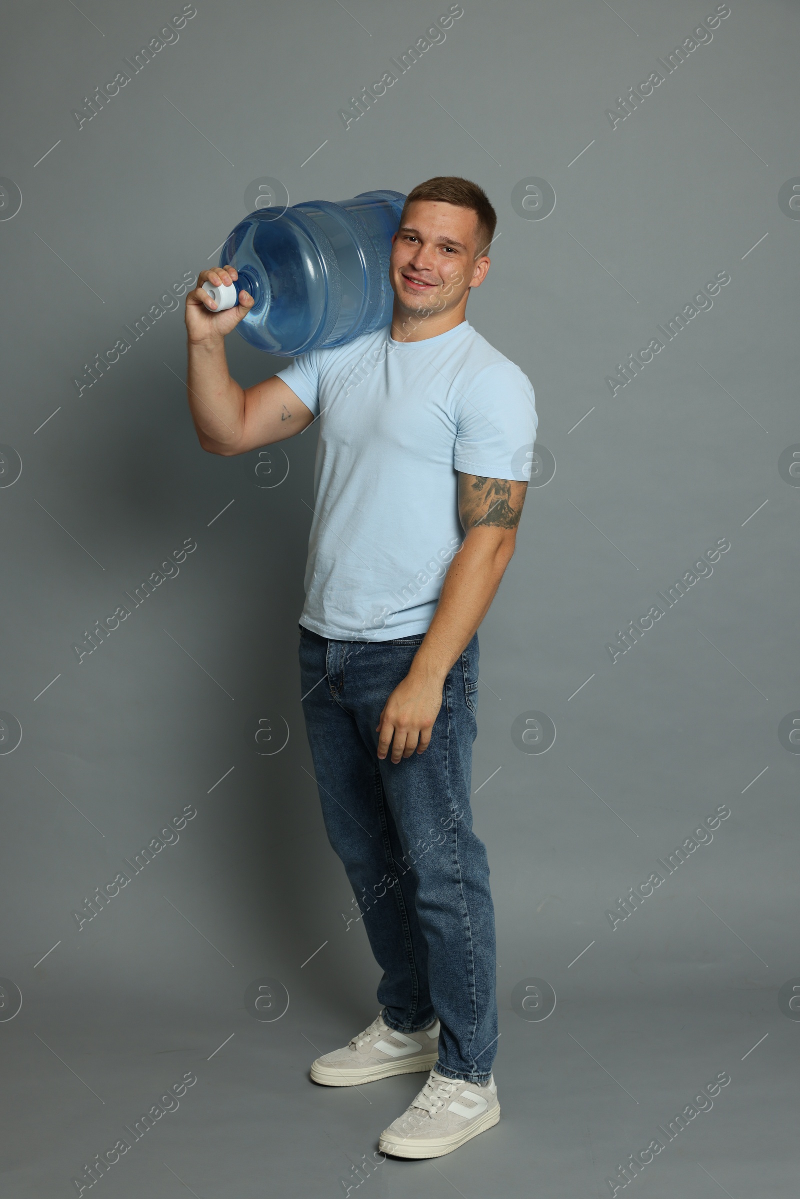 Photo of Smiling delivery man with cooler bottle of water on grey background