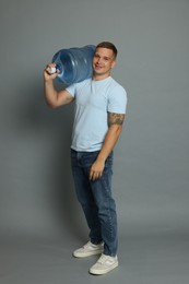 Photo of Smiling delivery man with cooler bottle of water on grey background