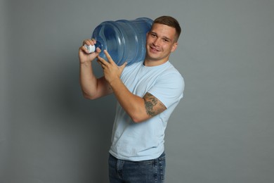 Photo of Smiling delivery man with cooler bottle of water on grey background