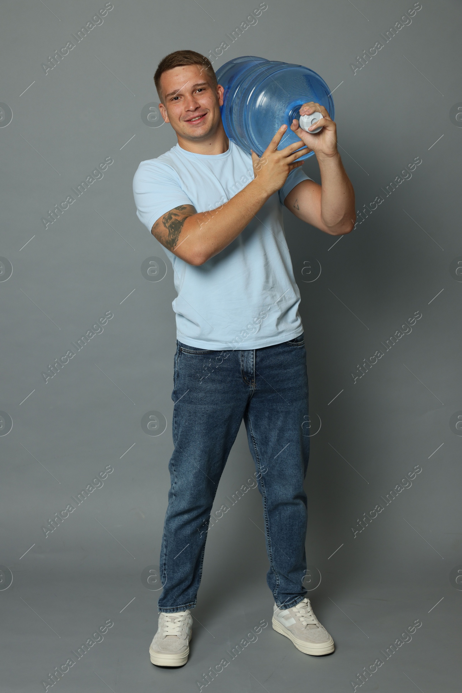 Photo of Smiling delivery man with cooler bottle of water on grey background